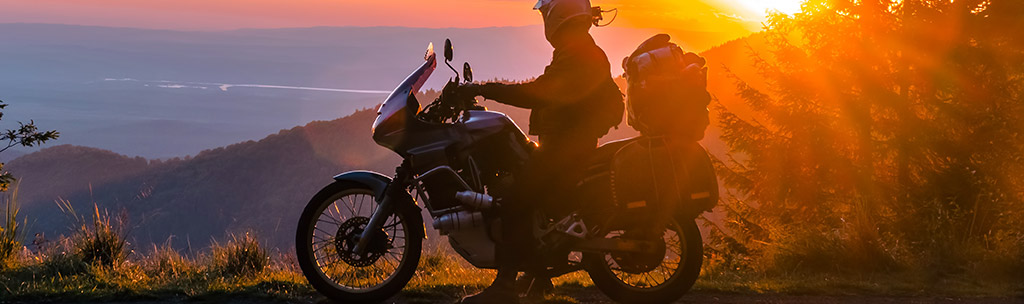 The profile of a biker on their motorcycle at the top of a mountain during sunset