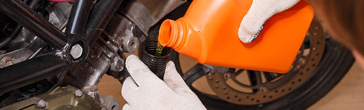 close up of someone pouring oil in his tank with an orange oil container