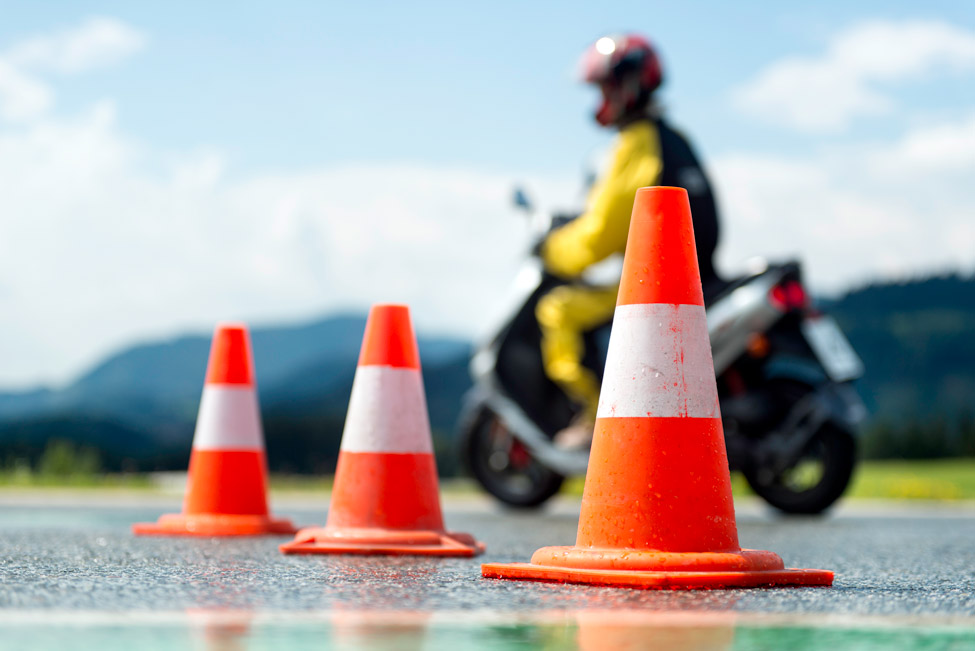 Photo of traffic cones in the foreground and a person on a motorcycle in the background