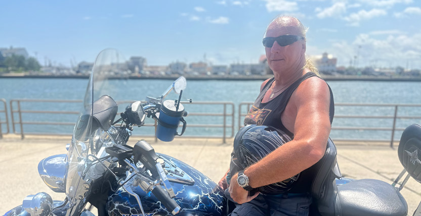Photo of a man sitting on a motorcycle. He is parked on a path overlooking a body of water.