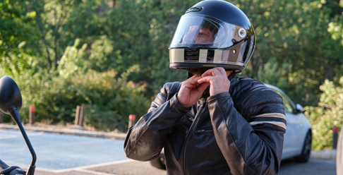 Photo of a man buckling a motorcycle helmet sitting on a motorcycle