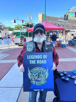 Photo of a white man holding a "legends of the road" sign