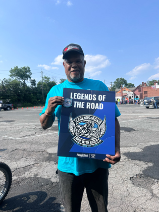Photo of a man holding a "legends of the road" sign