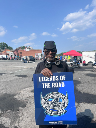 Photo of a man holding a "legends of the road" sign