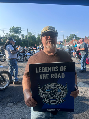 Photo of a man holding a "legends of the road" sign