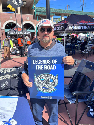 Photo of a man holding a "legends of the road" sign