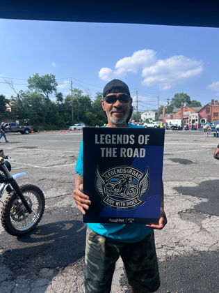 Photo of a man holding a "legends of the road" sign