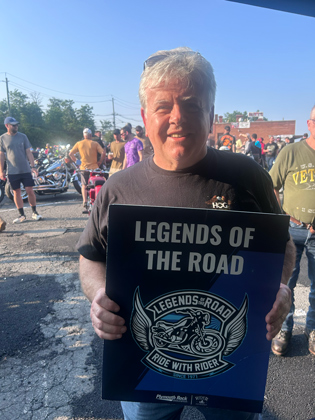 Photo of a man holding a "legends of the road" sign