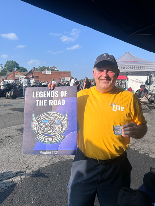 Photo of a man holding a "legends of the road" sign