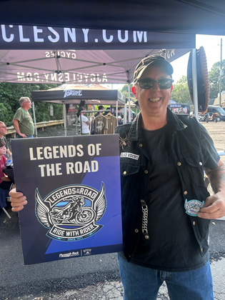 Photo of a man holding a "legends of the road" sign