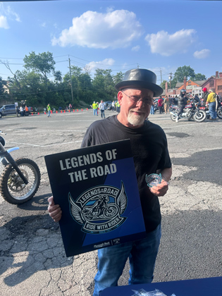 Photo of a man holding a "legends of the road" sign