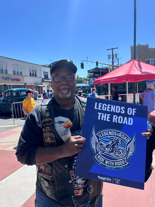 Photo of a man holding a "legends of the road" sign