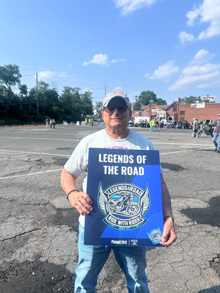 Photo of a man holding a "legends of the road" sign