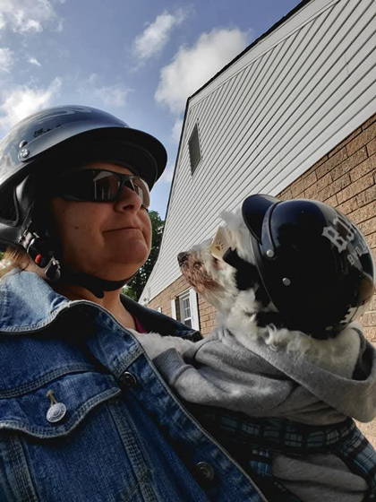 Photo of a woman wearing a helmet holding a small dog, also wearing a helmet