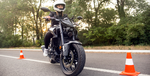 Photo of a person wearing a helmet on a motorcycle in a parking lot with cones