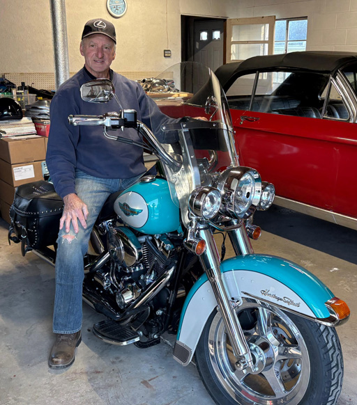 Photo of a man in a garage sitting on a blue motorcycle