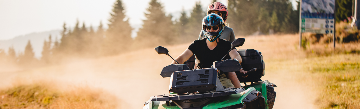 Photo of two people riding on one ATV down a dusty road