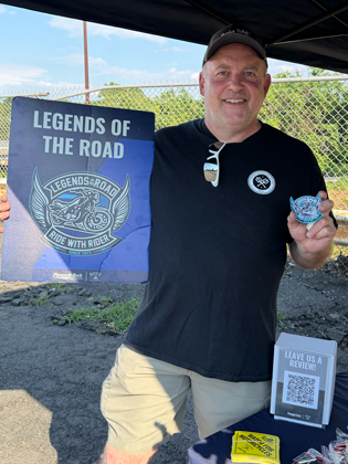 Photo of an older white man holding a sign that says "legends of the road"