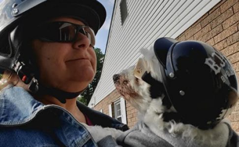 Photo of a woman wearing a helmet holding a small dog, also wearing a helmet