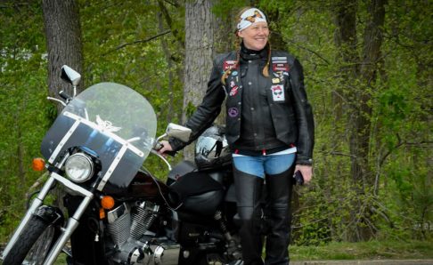 Liz-Pippi-Shay photo of a woman standing in the woods next to a motorcycle