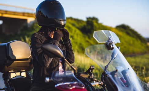 Photo of a person sitting on a motorcycle buckling a helmet